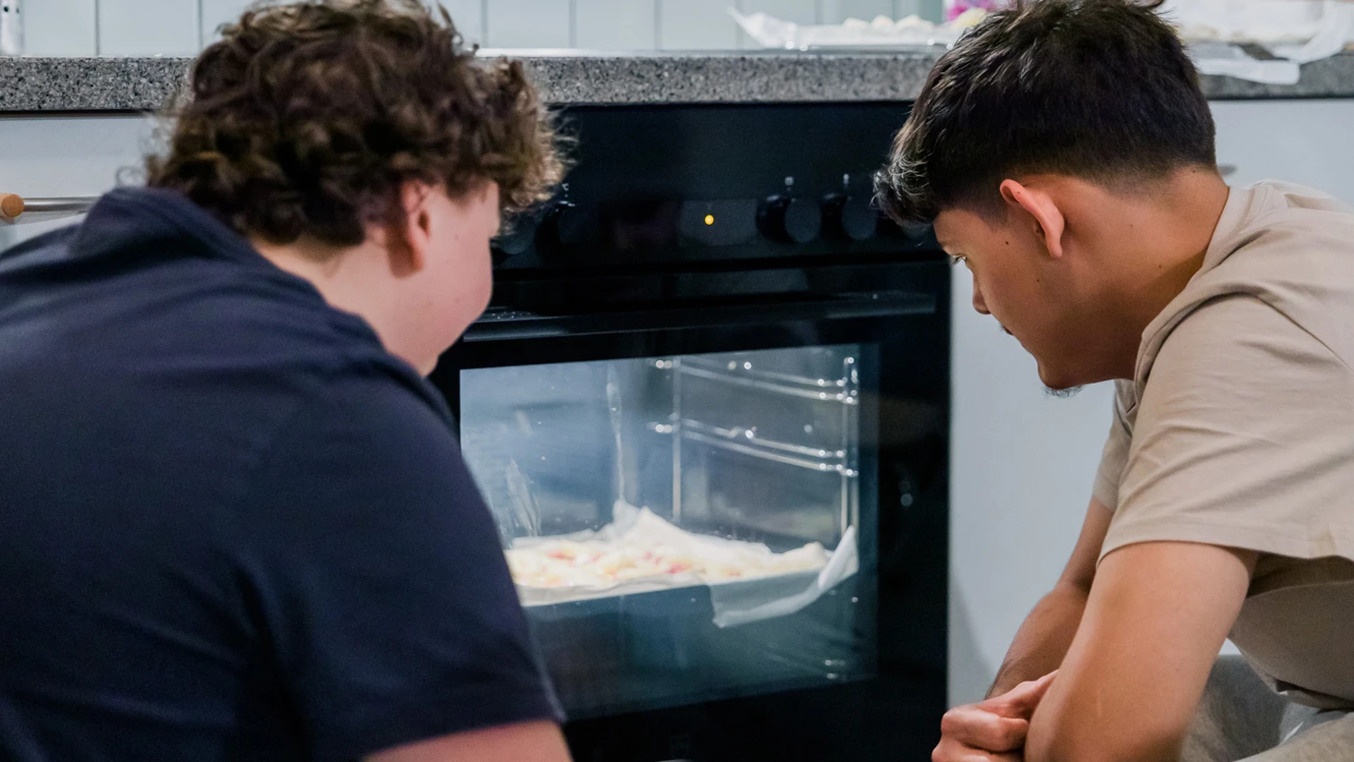 Deux jeunes accroupis devant un four qui chauffe une pizza.